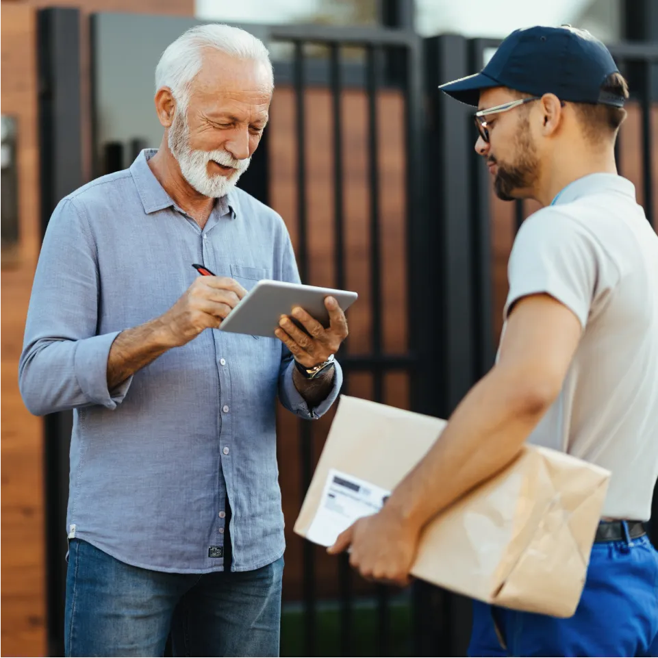 An elderly man signs for a package from a delivery man.