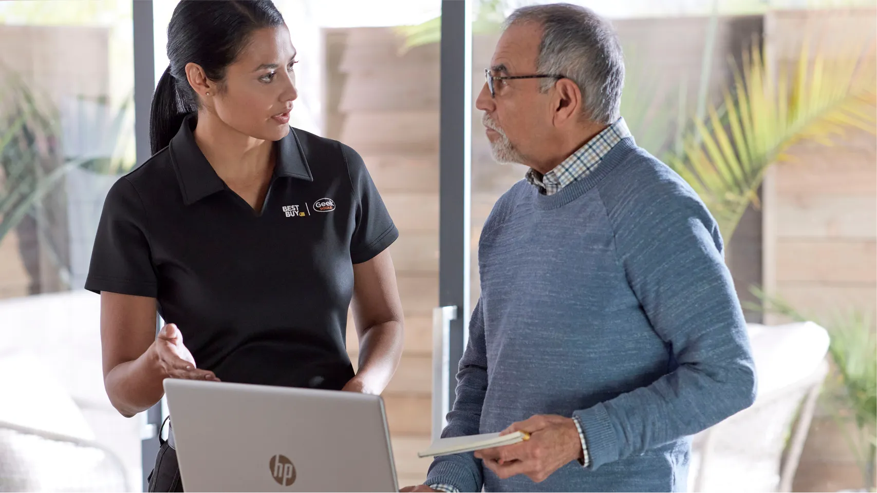A Geek Squad agent assists an elderly customer with an HP computer in his home.