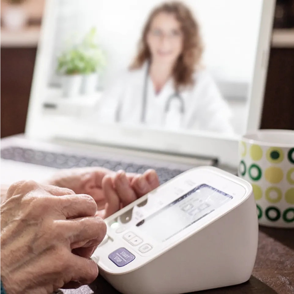 Elderly hands use a device while talking to a doctor on the computer.