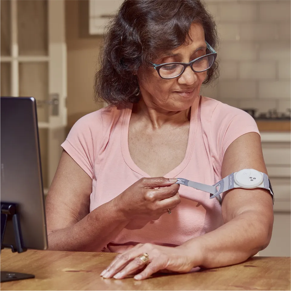 An elderly woman wraps a Current Health Continuous Vital Sign Monitor around her arm to measure her vital signs.