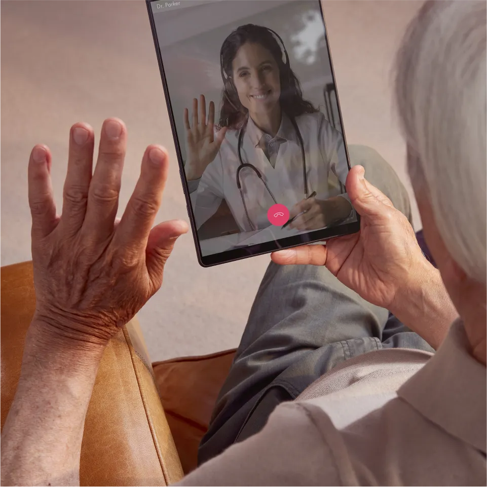 An elderly person waves to his doctor during a tele-appointment.