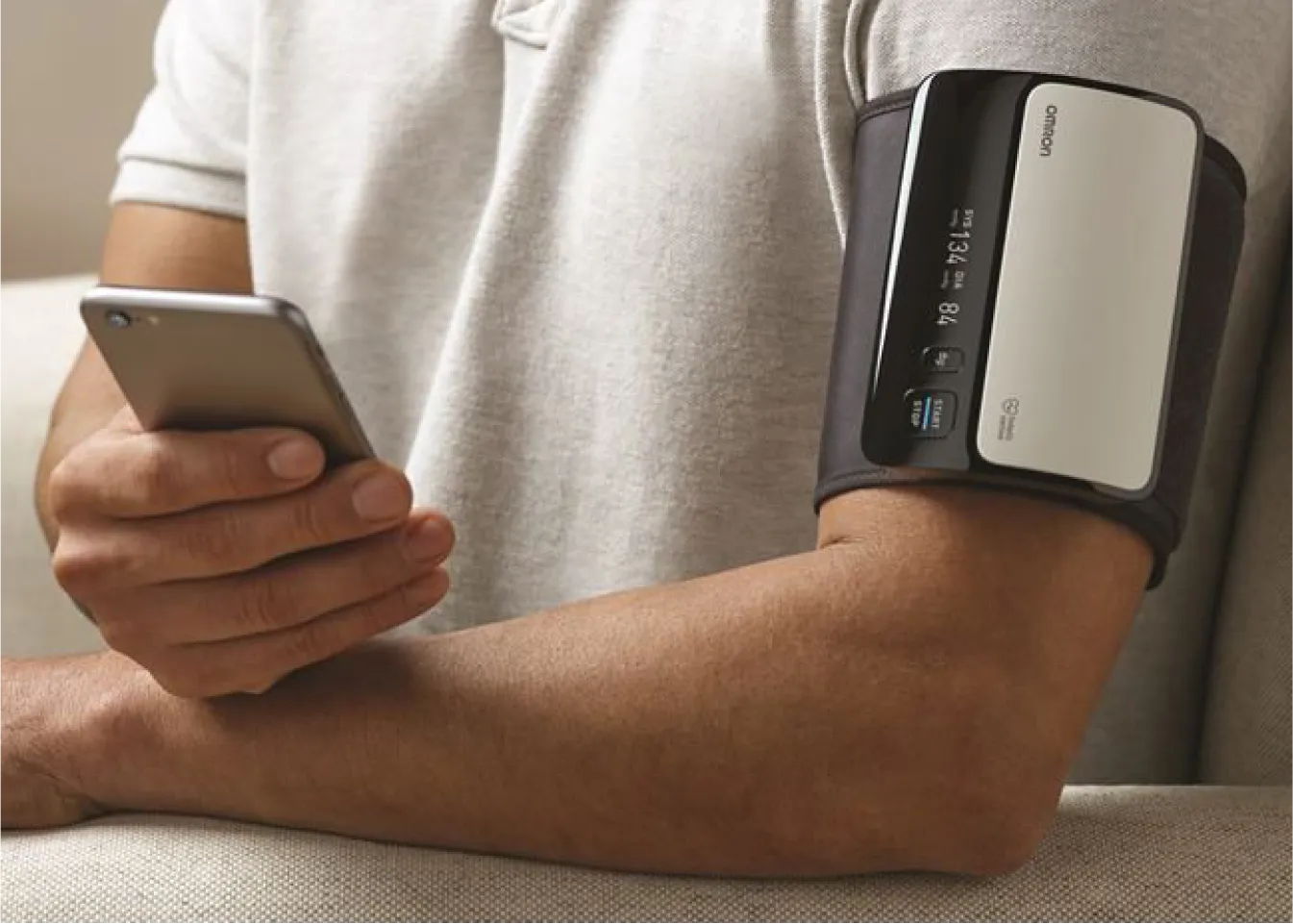 A blood pressure cuff is on one arm while the other hand holds a phone.
